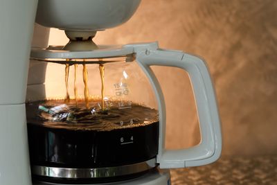 Photograph of a dripping, half-full white coffee pot on brown background