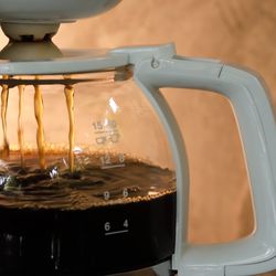 Photograph of a dripping, half-full white coffee pot on brown background