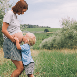 A pregnant woman, being kissed on the belly by a child.