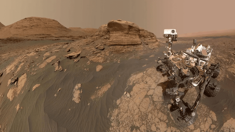 A mosaic produces a selfie of Curiosity with behind a nose structure, a layer protruberance of rock.