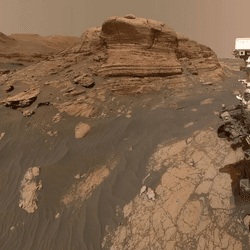 A mosaic produces a selfie of Curiosity with behind a nose structure, a layer protruberance of rock.