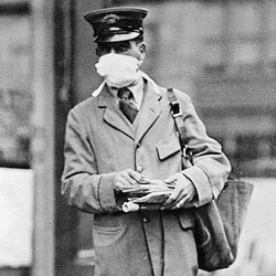 black and white photo of a man in a uniform, possibly a postman, wearing a white mask during the flu pandemic of 1918-1920